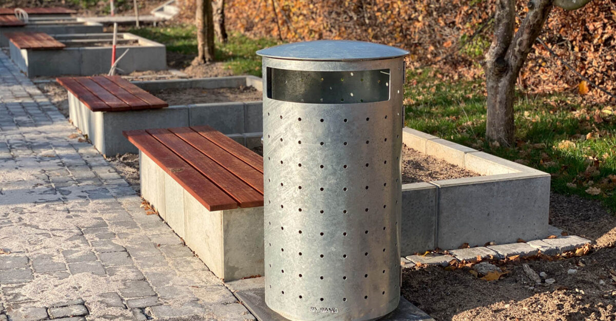 en stor undendørs affaldsspand i unkt design leveret i galvaniseret stål samt en beton plantekasse med beklædning i mahgni planker