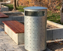 en stor undendørs affaldsspand i unkt design leveret i galvaniseret stål samt en beton plantekasse med beklædning i mahgni planker
