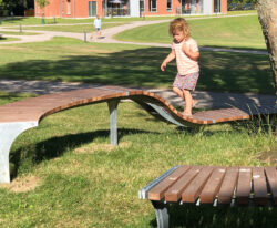 et barn løber på en special bænk i galvaniseret stål og beklædt med mahogni stave rundt om et træ i Odders Vitapark