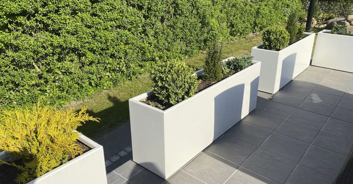 Smukke plantekummer og plantekasser i galvaniseret og malet stål står i en privat have