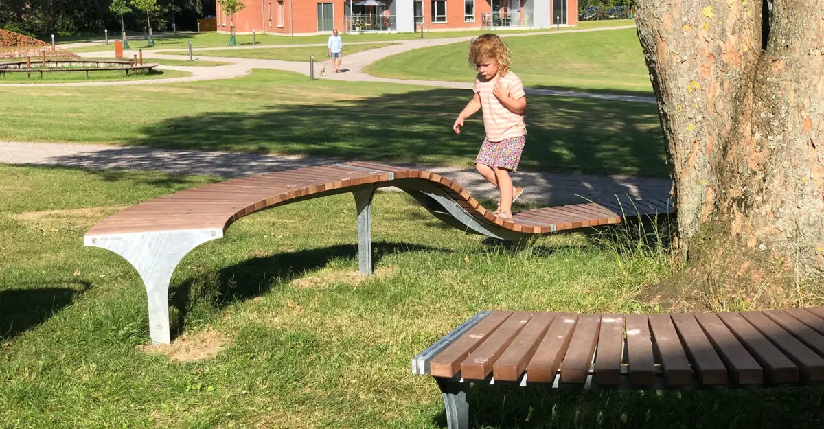 et barn løber på en special bænk i galvaniseret stål og beklædt med mahogni stave rundt om et træ i Odders Vitapark